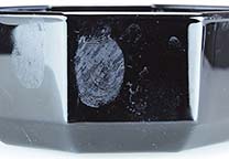 Fingerabdrücke mit Blut auf einem schwarzen Glasgegenstand und mit Schräglicht fotografiert.